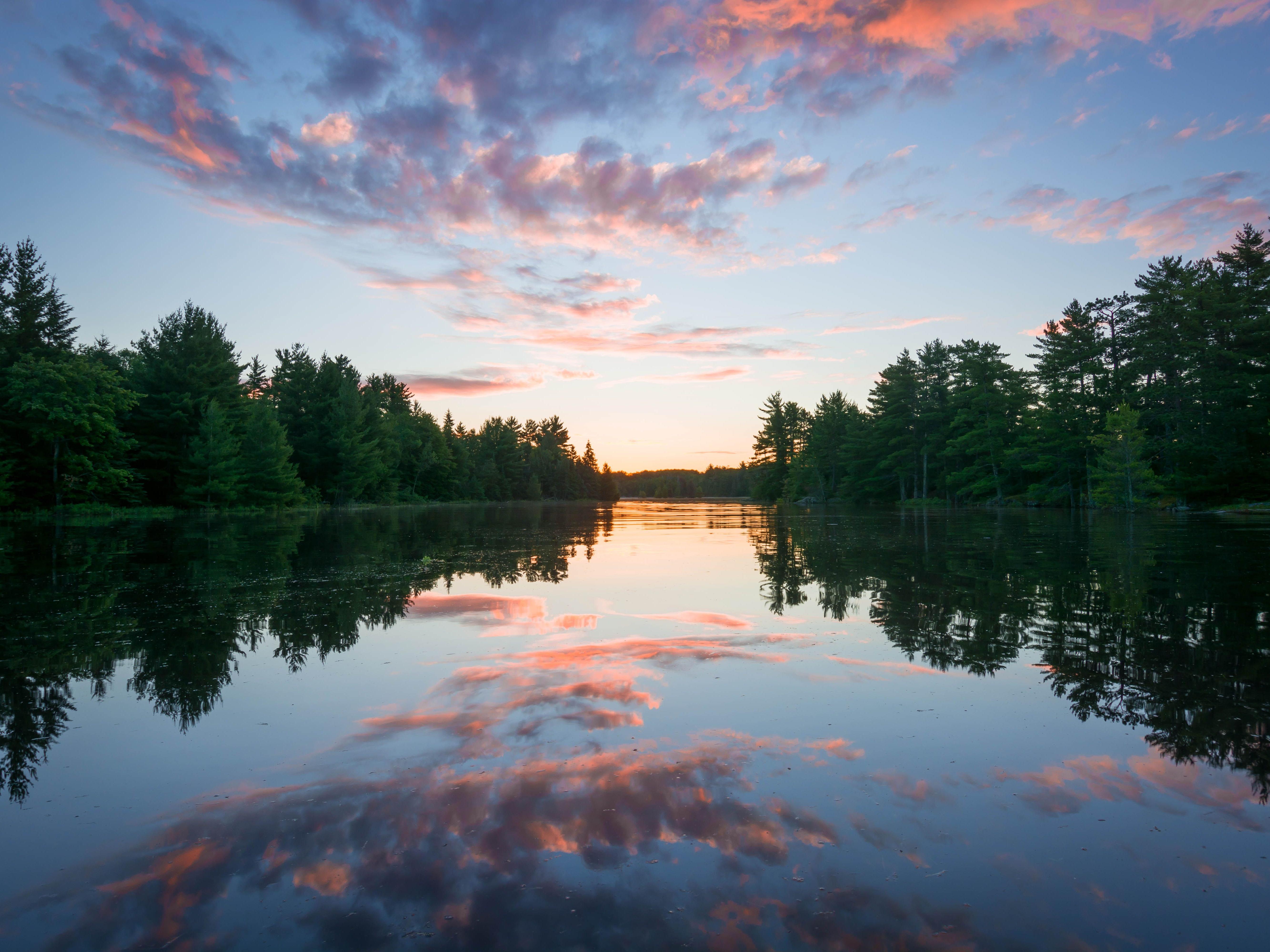 A real photograph of a calm sunset over Rainy Lake in Voyageurs National Park with a glowing orange sky reflected on the water and dark island silhouettes