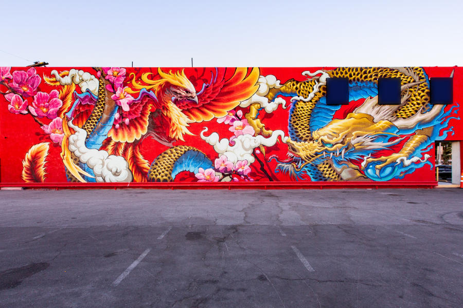 A real photograph of a colorful mural on a building in the Las Vegas Arts District, with a quiet street and a few pedestrians nearby