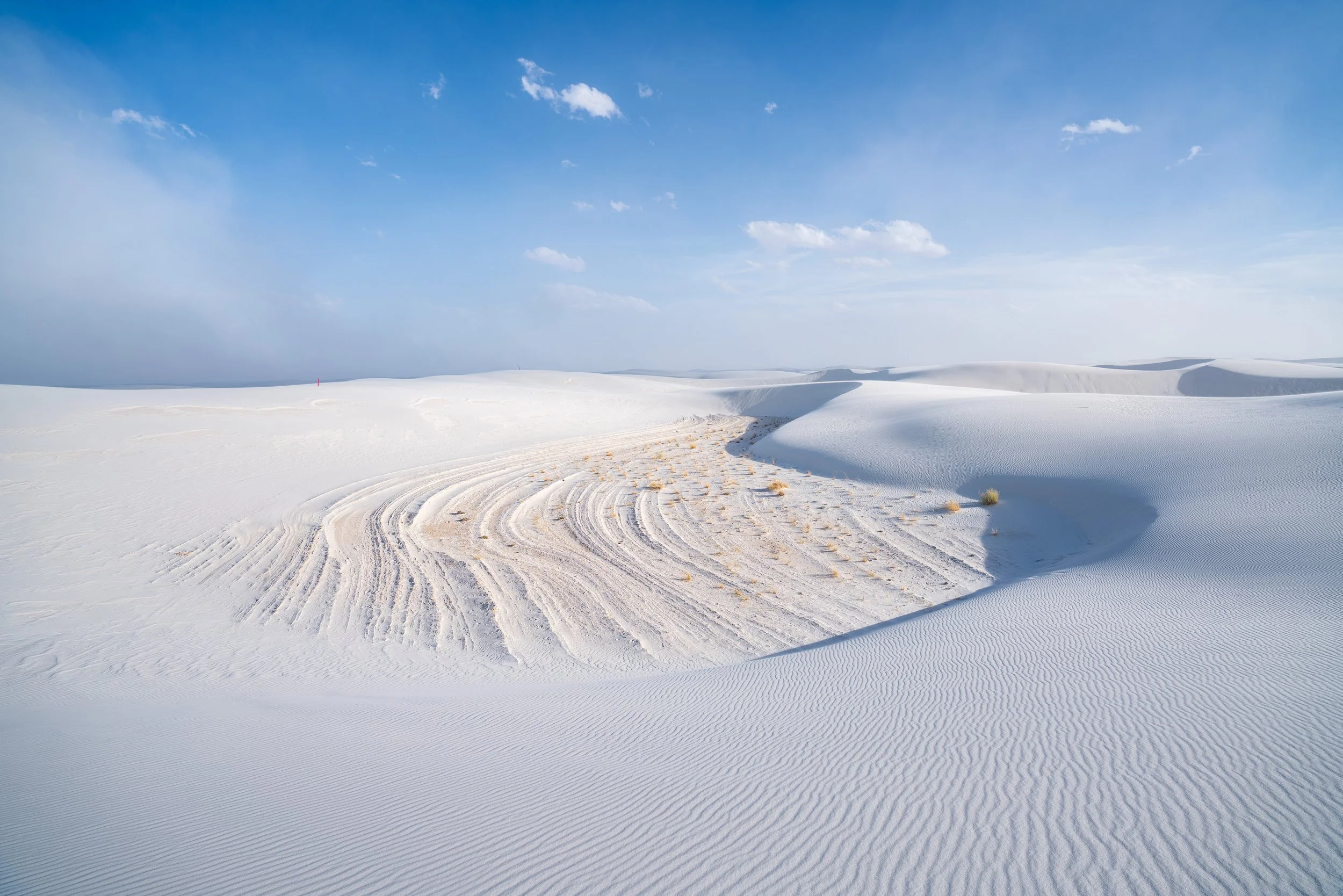 A real photograph of a couple of hikers walking along a marked route across white dunes on the Alkali Flat Trail at White Sands National Park