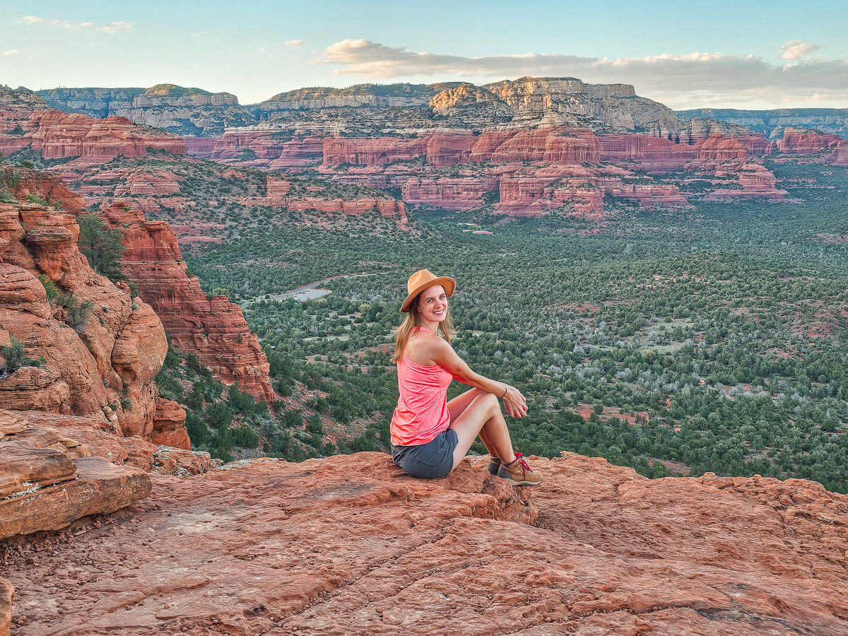 A real photograph of a hiker sitting on the flat top of Doe Mountain in Sedona looking out over red rock buttes and green desert vegetation, late afternoon golden light, scenic travel photography