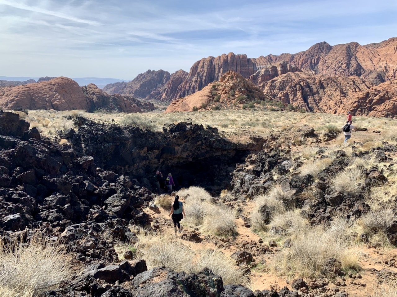A real photograph of a hiking trail winding between red sandstone formations and dark lava rock in Snow Canyon State Park under bright daylight