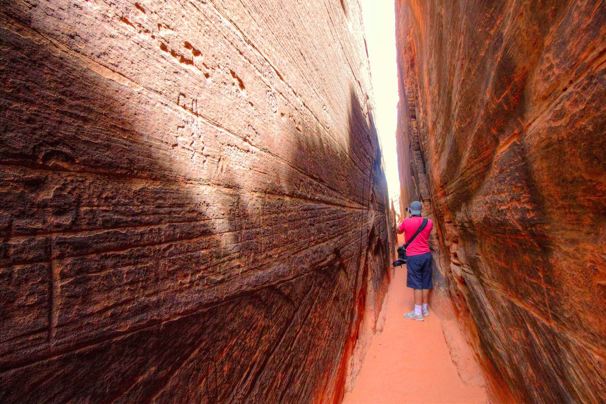 A real photograph of a narrow sandstone slot canyon corridor in Snow Canyon State Park with warm light on the walls and a sandy floor