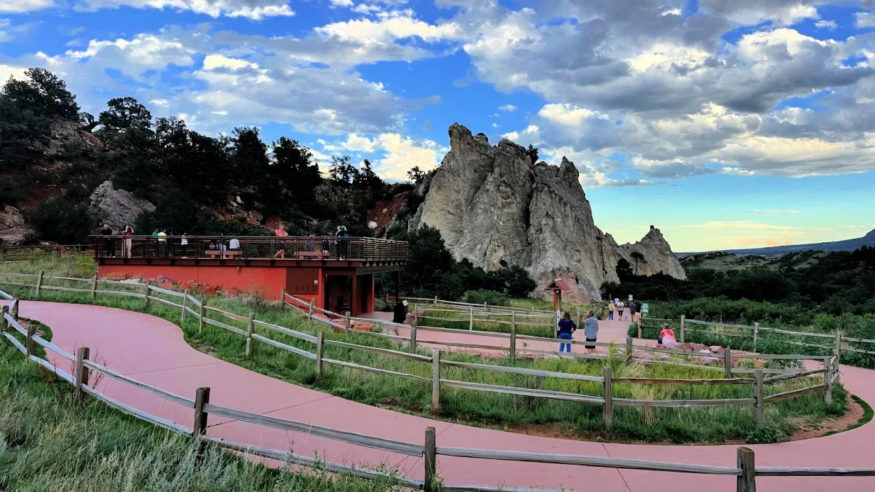 A real photograph of a paved overlook area at Garden of the Gods with red rock formations in view and ample space for wheelchairs and walkers