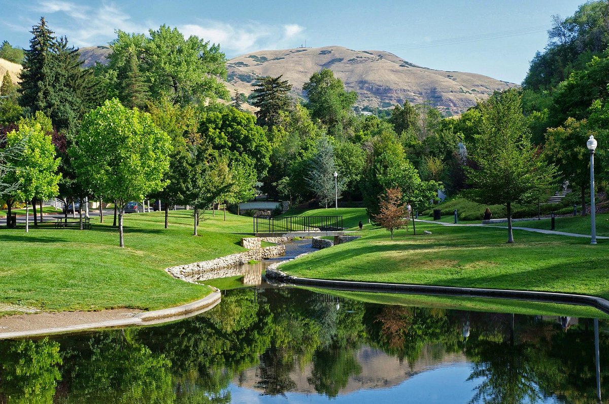 A real photograph of a paved walking path in Memory Grove Park in Salt Lake City with trees, a small stream, and hikers walking toward the canyon