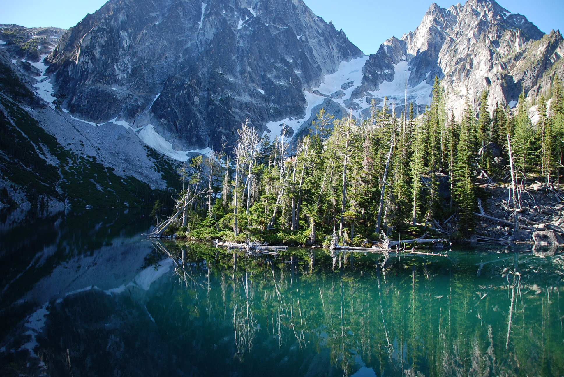A real photograph of a small backpacking tent set up on durable ground near Colchuck Lake in Washington, with evening light on Dragontail Peak in the background
