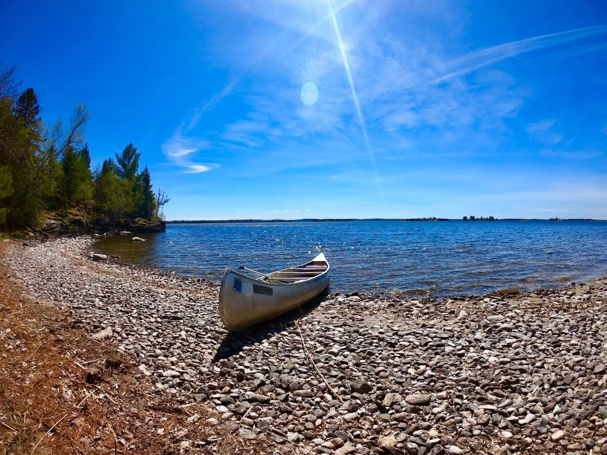 A real photograph of a small motorboat cruising on Kabetogama Lake with evergreen islands and a bright blue summer sky in Voyageurs National Park
