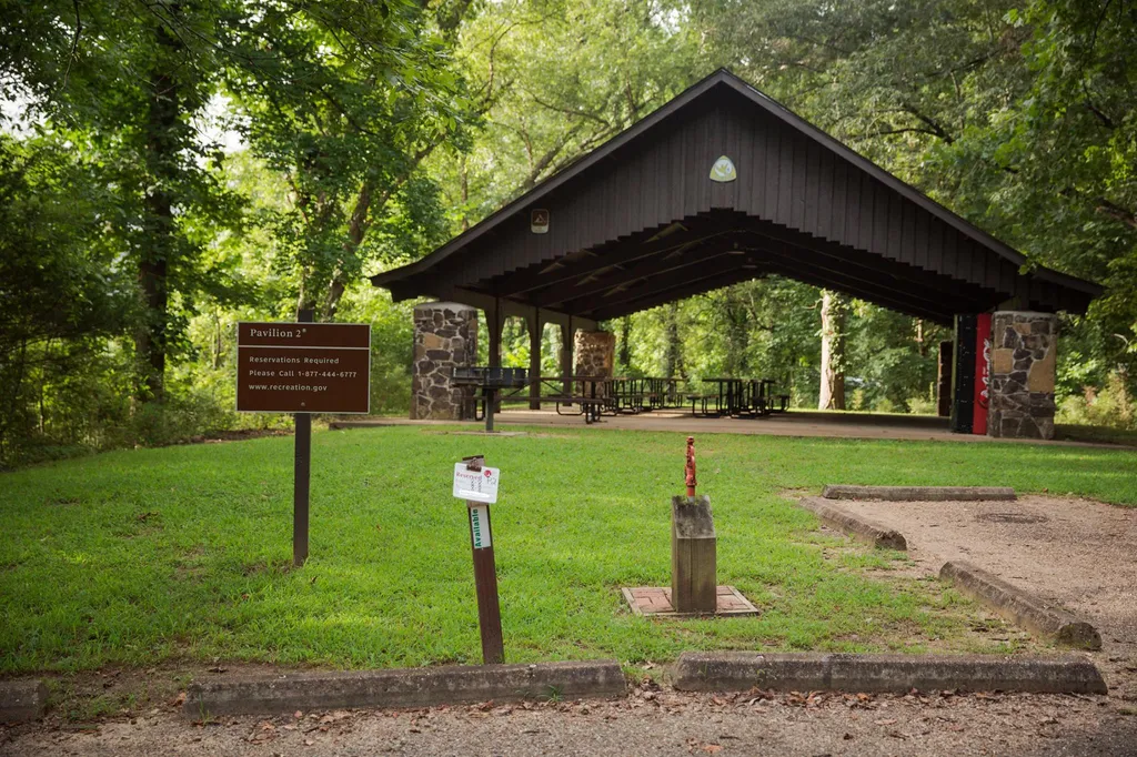 A real photograph of a small picnic setup on a wide gravel bar beside the Buffalo National River, with a cooler in the shade and clear shallow water nearby