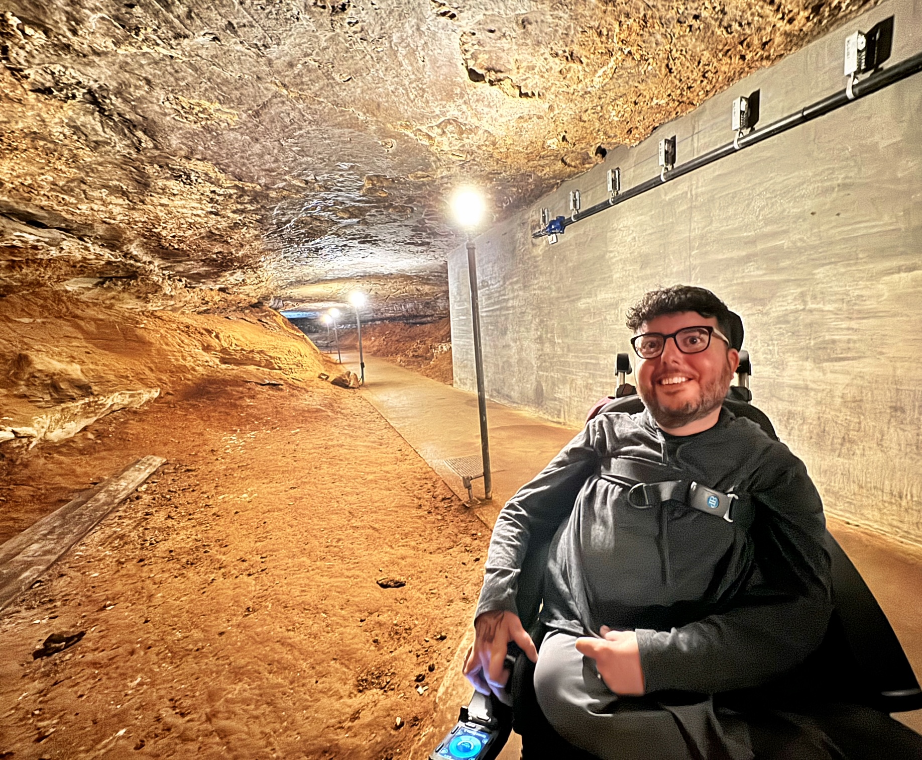 A real photograph of a traveler standing outside in a wooded parking area near Mammoth Cave, holding a light jacket with hands free and no backpack, ready for a cave tour