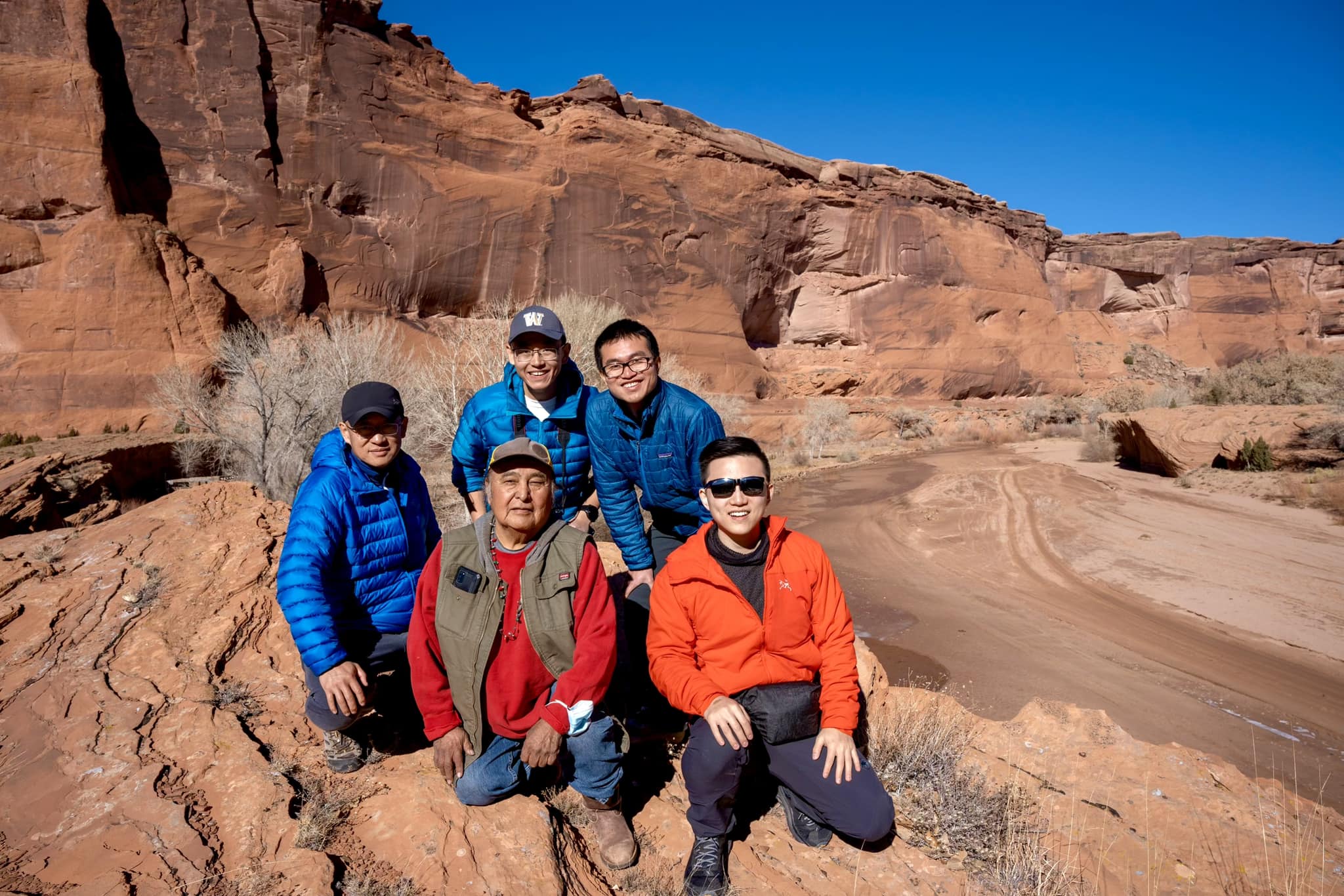 A real photograph of an authorized tour vehicle on the sandy canyon floor at Canyon de Chelly, with tall red sandstone walls rising on both sides and sparse desert vegetation