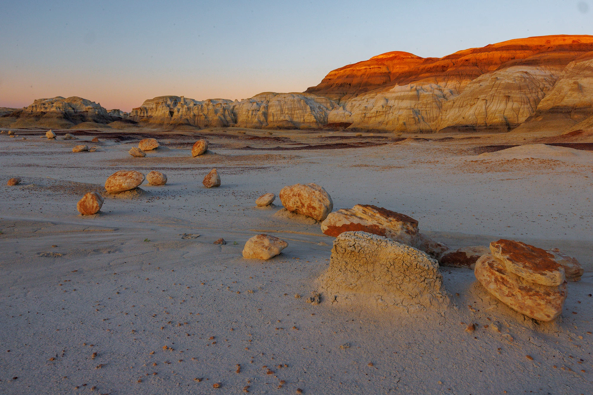 A real photograph of boots with thick bentonite clay stuck to the soles on a muddy badlands surface after rainfall