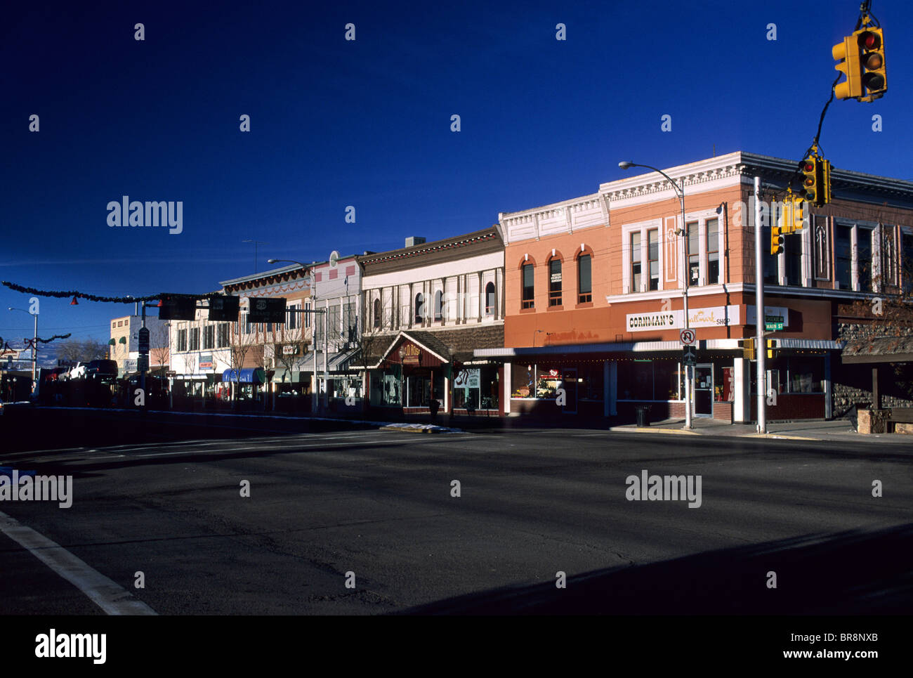A real photograph of downtown Montrose, Colorado in the evening with storefronts lit up, a calm main street, and distant hints of the San Juan Mountains