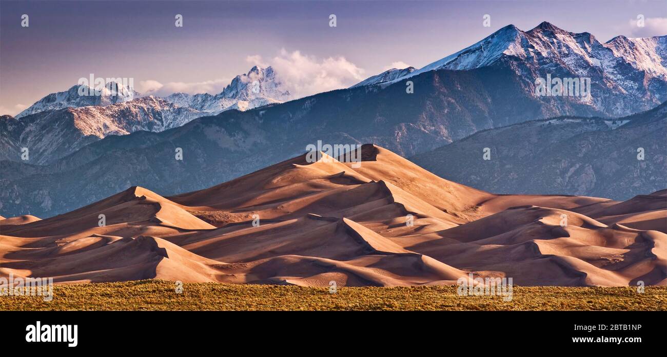 A real photograph of golden sunrise light hitting the sand dunes at Great Sand Dunes with the Sangre de Cristo Mountains under a clear morning sky