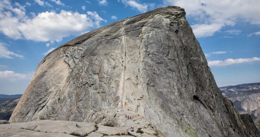 A real photograph of hikers climbing the steep stone steps on the Subdome approach in Yosemite National Park on a bright day