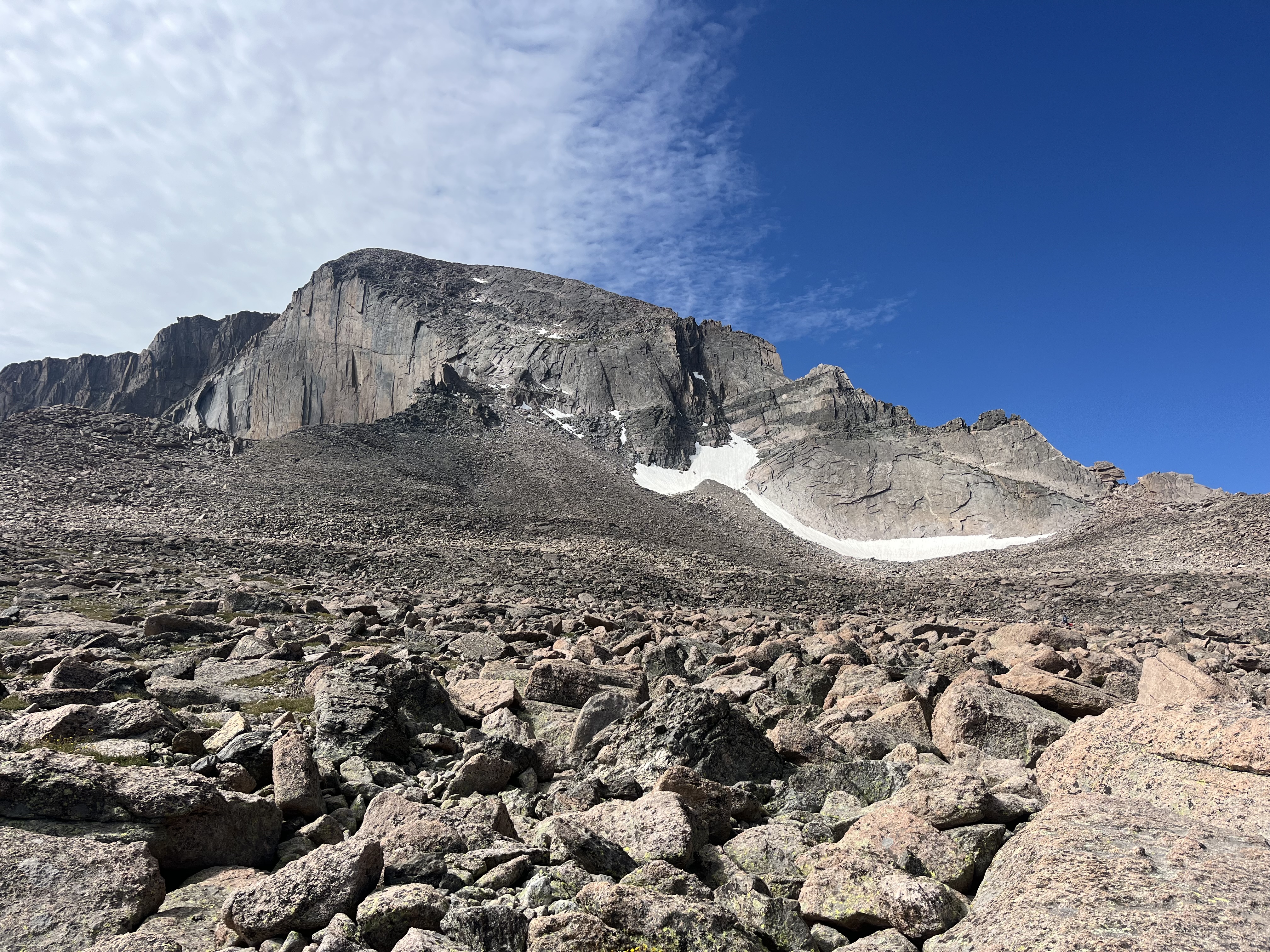 A real photograph of hikers on the Longs Peak Keyhole Route near the Keyhole notch, wearing helmets and climbing over rocky terrain with expansive views behind them