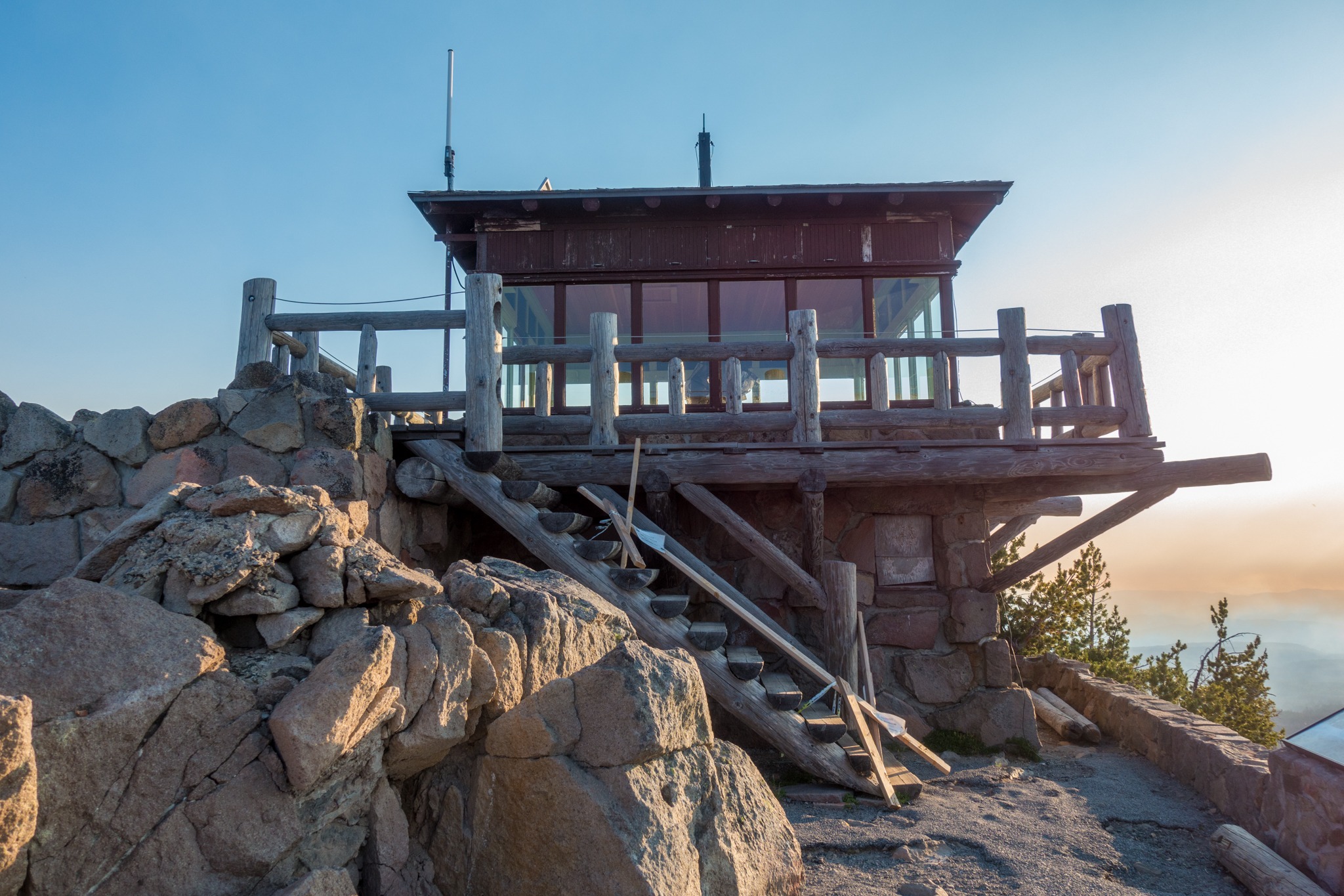A real photograph of hikers walking up the Watchman Peak trail with volcanic rock along the path and Crater Lake visible in the distance
