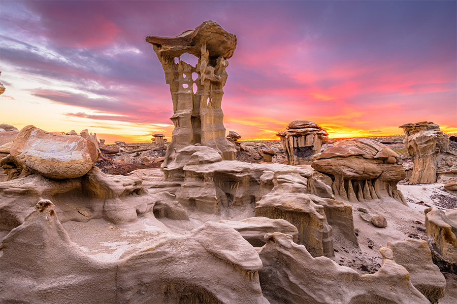 A real photograph of pale, eroded Bisti Badlands hoodoos and cracked clay flats glowing at sunrise under a wide New Mexico sky