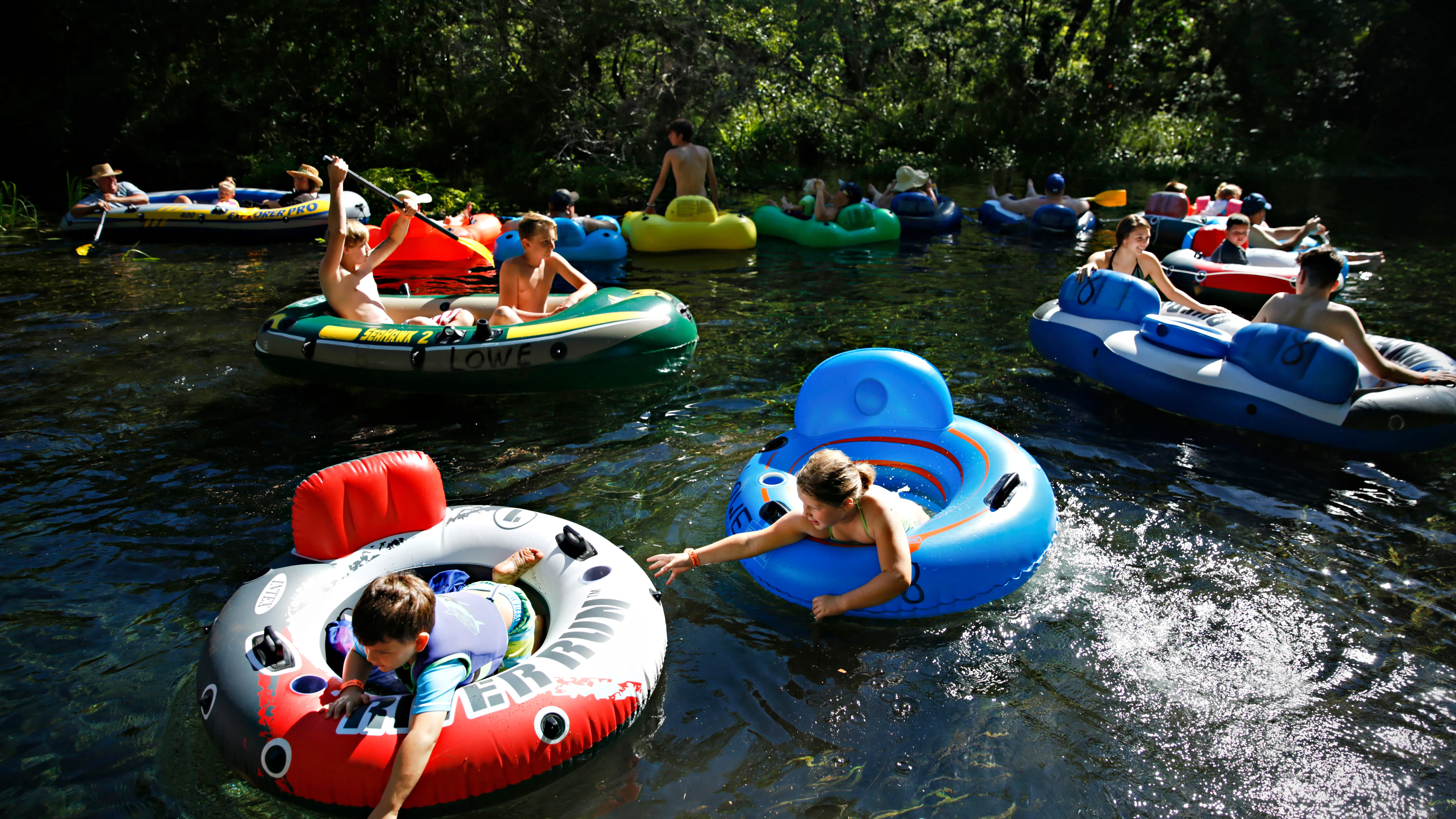 A real photograph of people floating in inner tubes down a clear spring fed river in Florida, surrounded by green trees on a sunny day