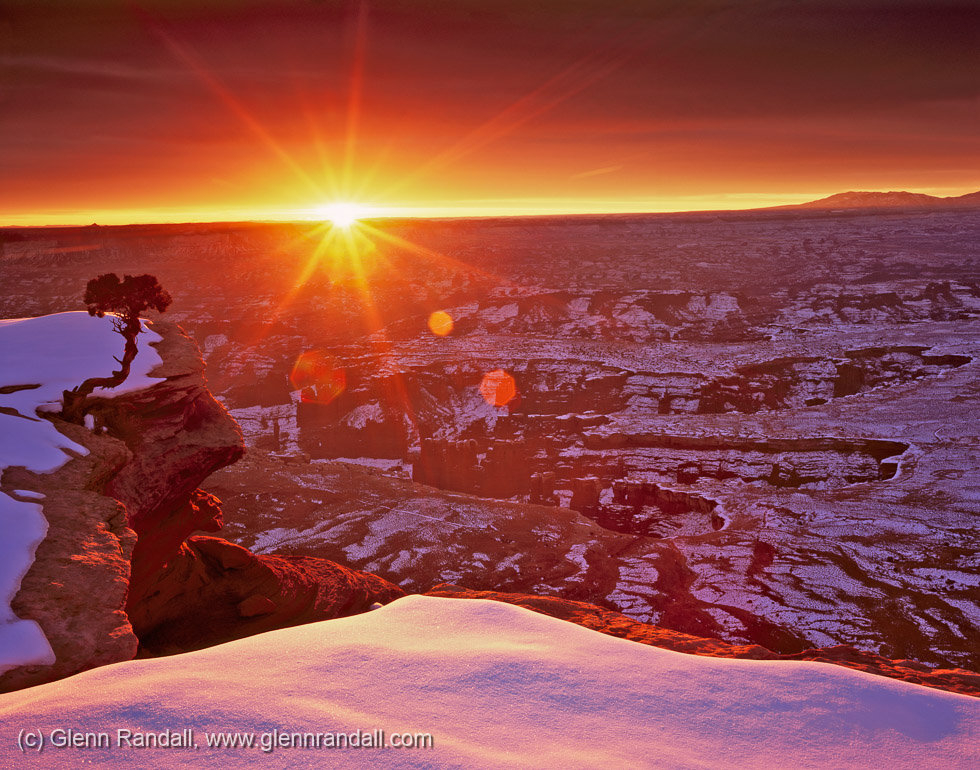 A real photograph of sunrise light spilling across Canyonlands National Park from Grand View Point in Island in the Sky, with layered red rock mesas and deep canyons fading into the distance