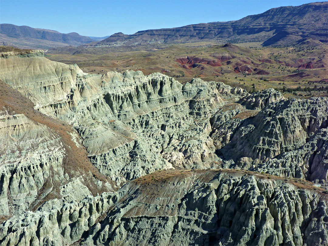 A real photograph of the Blue Basin area in the Sheep Rock Unit, with pale blue-green badlands and a narrow trail leading toward layered hills under bright sun
