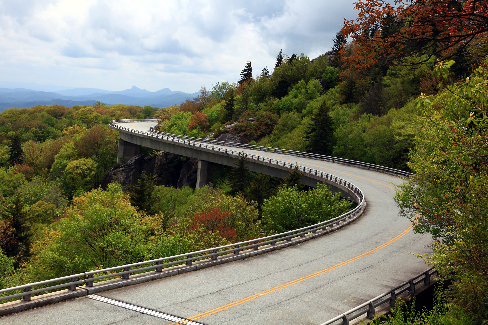 A real photograph of the Linn Cove Viaduct on the Blue Ridge Parkway, curving around the side of Grandfather Mountain with evergreen forest and rocky peaks behind