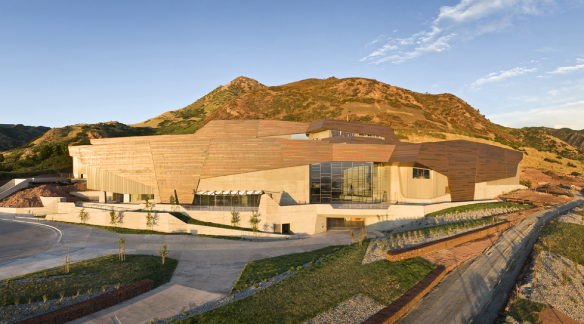 A real photograph of the Natural History Museum of Utah building in Salt Lake City with its copper-toned exterior, photographed in daylight with foothills and sky in the background