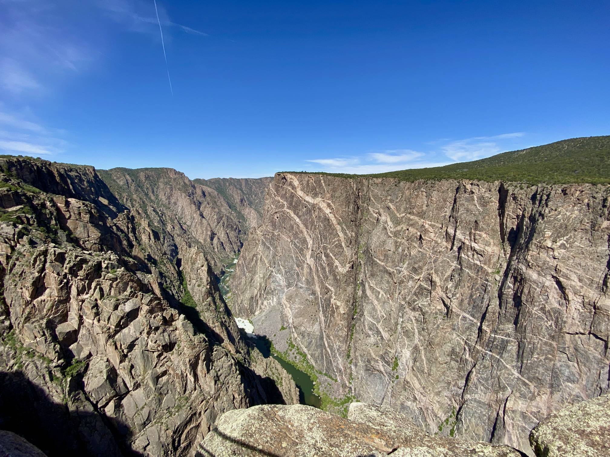 A real photograph of the Painted Wall cliff face in late afternoon light, showing steep vertical rock with subtle color bands and a deep canyon shadow below