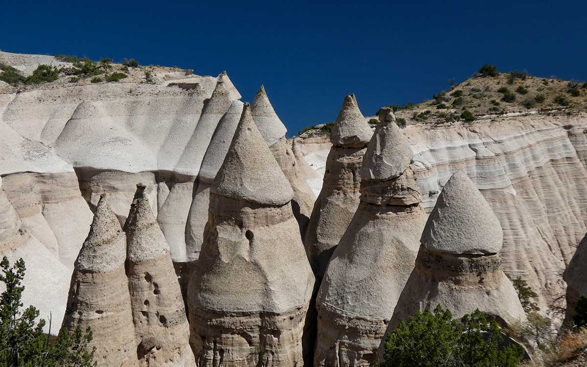 A real photograph of the cone-shaped tent rock formations at Kasha-Katuwe Tent Rocks National Monument, with pale tan spires under a deep blue New Mexico sky