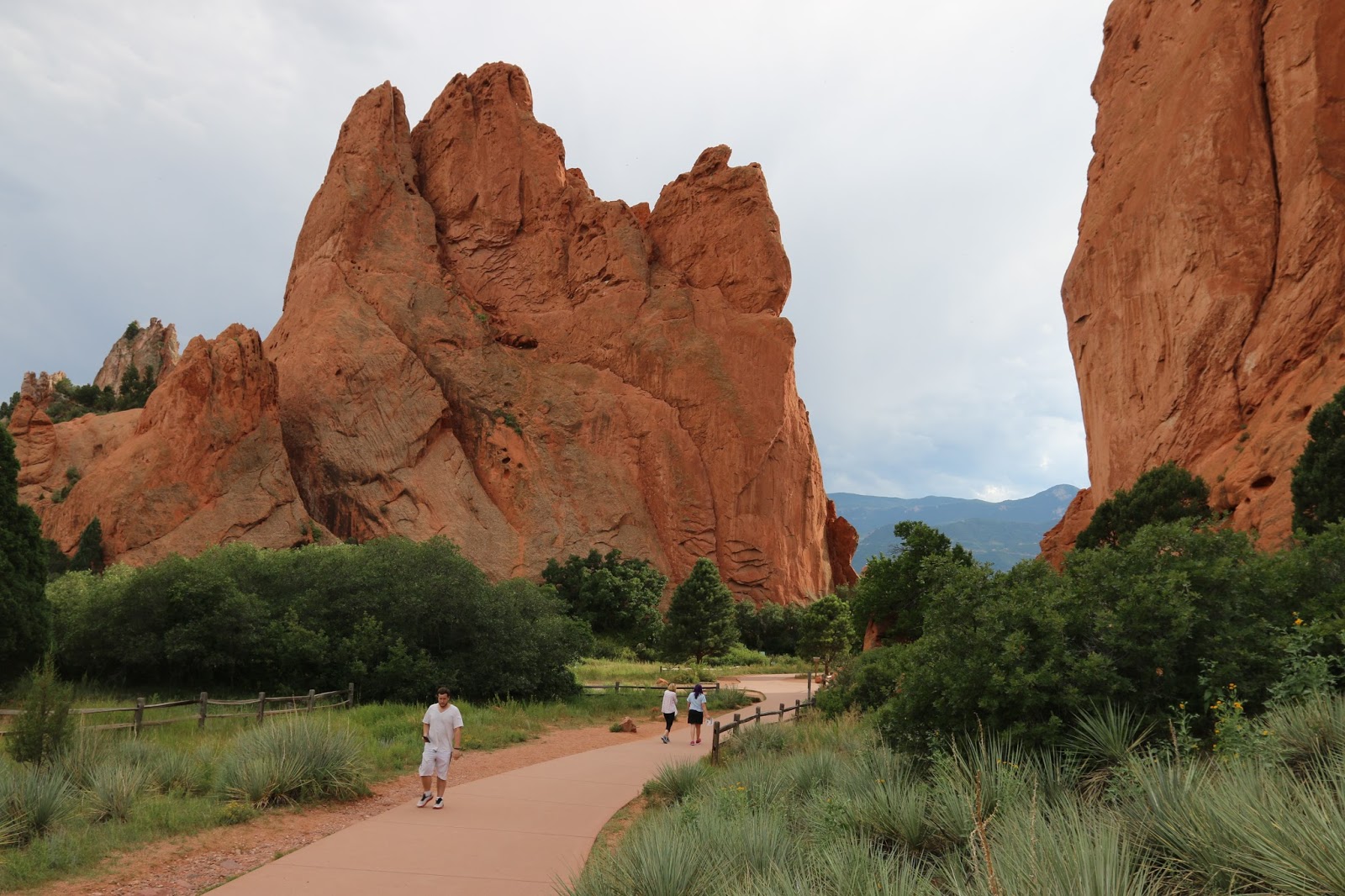 A real photograph of the paved Central Garden Trail winding between tall red sandstone fins with visitors walking at an easy pace