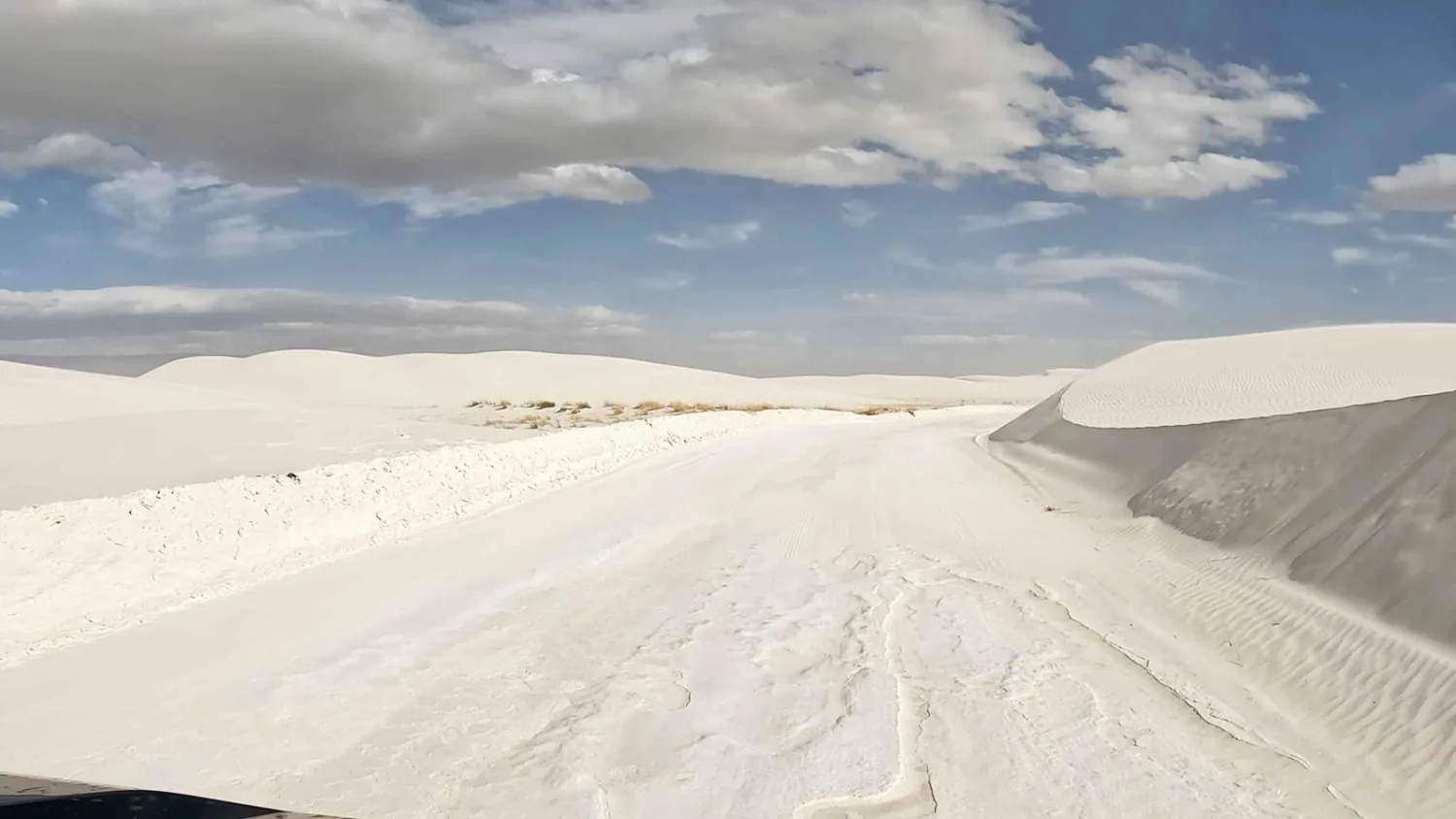A real photograph of the paved Dunes Drive curving through bright white gypsum dunes under a deep blue sky in White Sands National Park