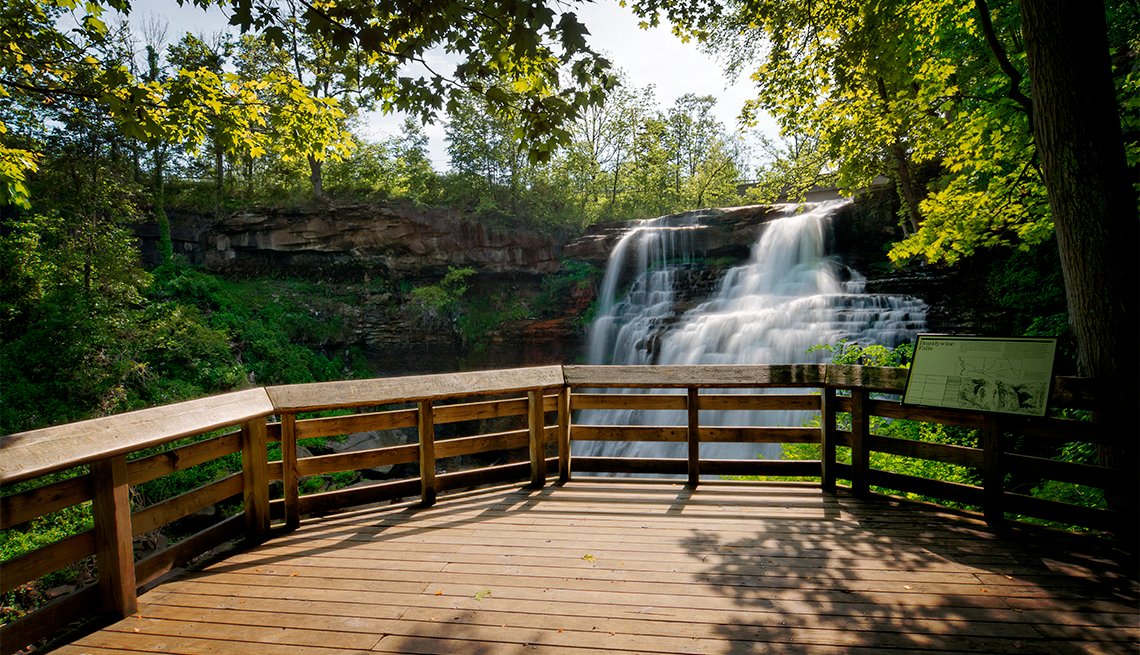 A real photograph of the wooden boardwalk and viewing platform at Brandywine Falls, with visitors standing at the rail looking into the forested gorge
