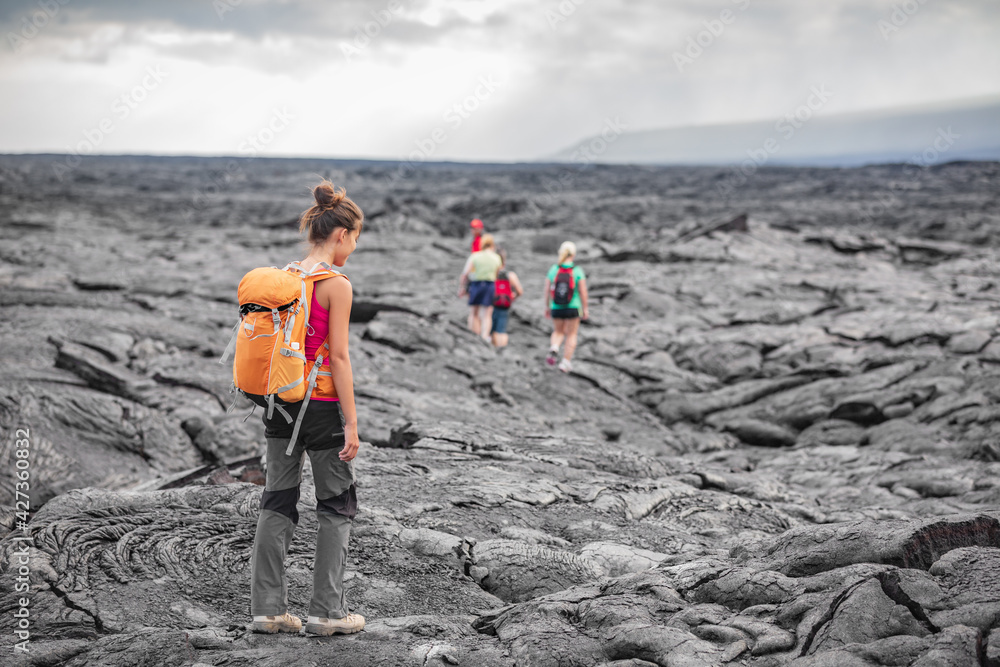 A real photograph of two hikers wearing light rain jackets on a misty trail in Hawaiʻi Volcanoes National Park, with wet volcanic rock and low clouds in the background