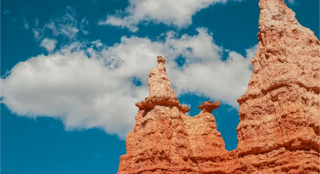 A real photograph on the Queens Garden Trail in Bryce Canyon showing a winding dirt path through clustered orange hoodoos under a bright blue sky