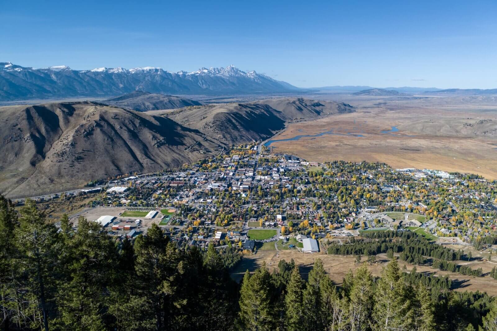 A real photograph taken from above showing the town of Jackson, Wyoming with the surrounding valley and mountains in the distance on a clear summer day