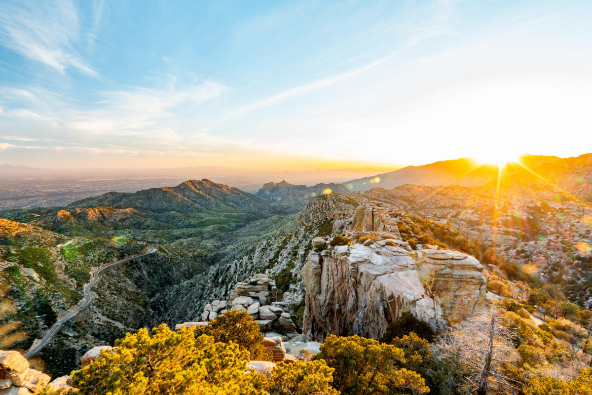 A real photograph taken from an overlook along the Catalina Highway showing the winding road cutting through rocky desert hills with Tucson visible in the hazy distance