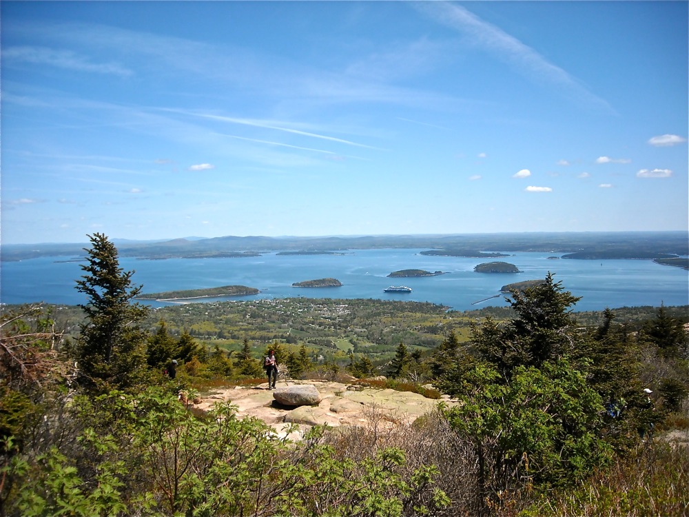 A real photograph taken in daylight from a Cadillac Mountain overlook in Acadia National Park, showing layered islands and blue ocean under a clear sky