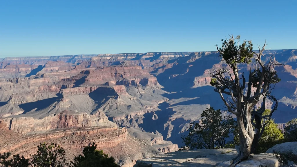 A real sunset photograph at Hopi Point on the Grand Canyon South Rim, with layered canyon walls glowing orange and purple and a few visitors standing near the rim railing