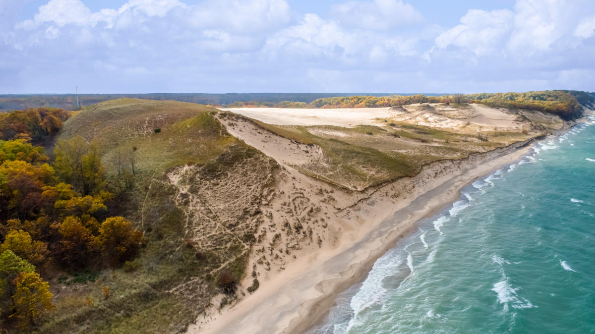 A sandy dune trail climbing toward a wide view of Lake Michigan with pale blue water and a bright sky at Indiana Dunes National Park