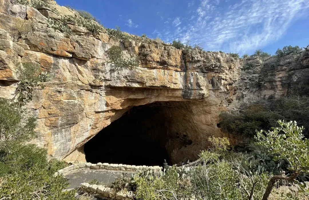 A short desert walking path near Carlsbad Caverns visitor area with rocky ground, low shrubs, and distant limestone hills under bright afternoon sun, realistic travel photo