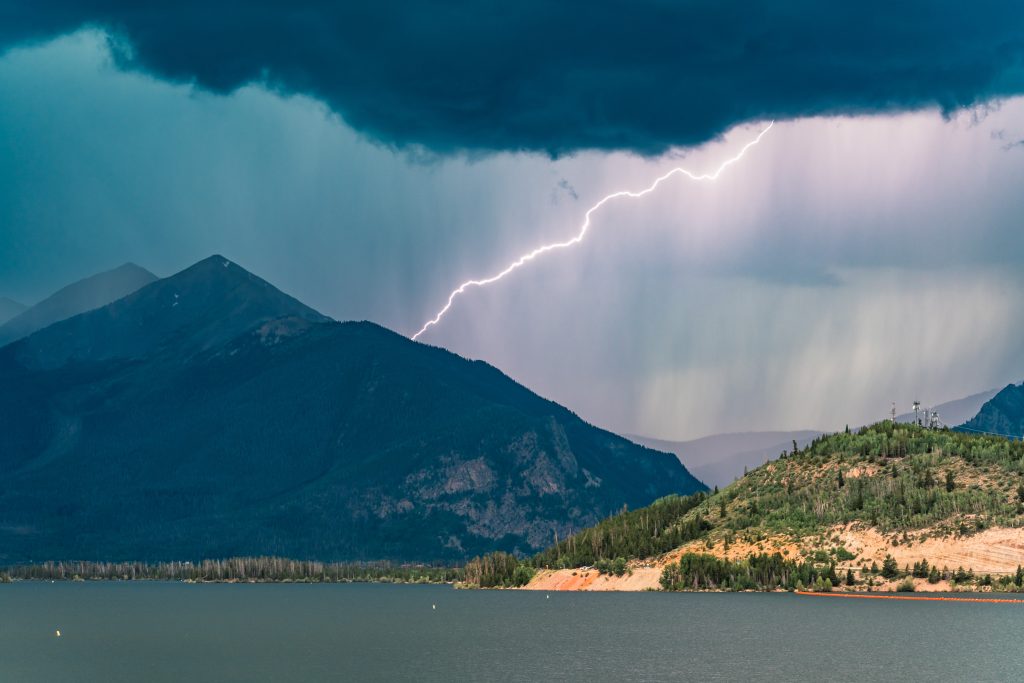 A single hiker descending from an exposed alpine ridge as dark thunderclouds build behind them in Rocky Mountain National Park, realistic outdoor photography