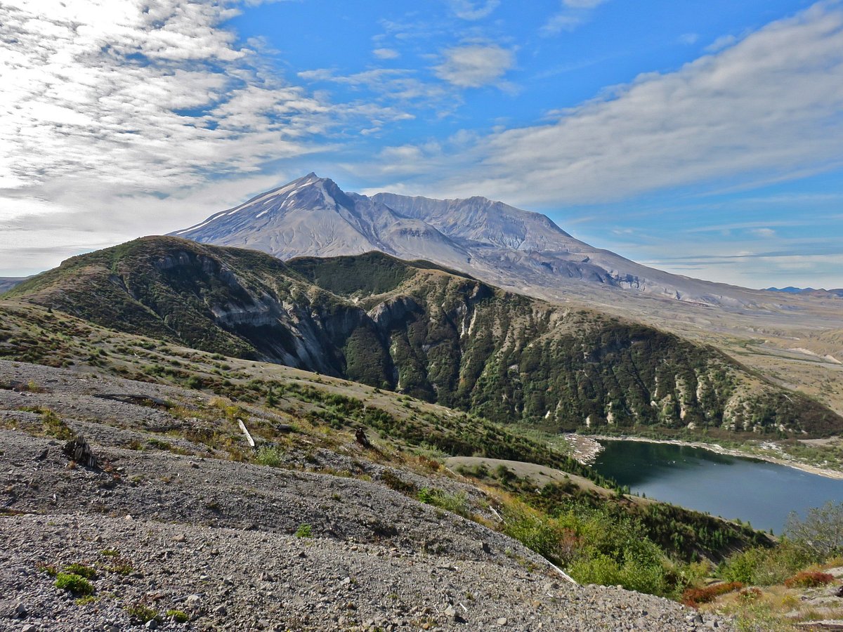 A single hiker on an exposed mountain ridgeline in the Rocky Mountains during a shoulder-season storm, wearing a hooded shell as wind-driven sleet moves across the trail, real photograph