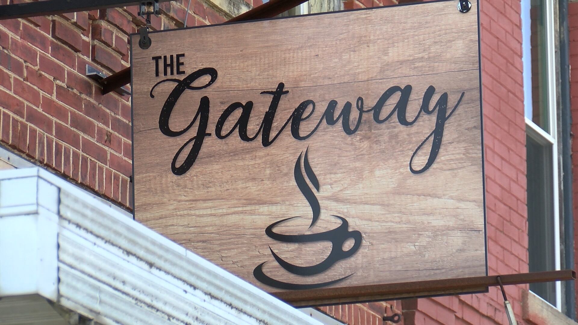 A single real photograph of a small coffee shop counter in a gateway town near a national park, with a barista making espresso and hiking boots visible near a chair