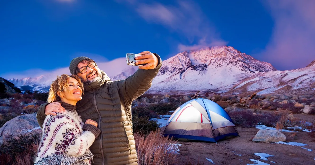 A small backpacking tent pitched on a high alpine bench at sunset with snow-capped peaks in the background, real photography style