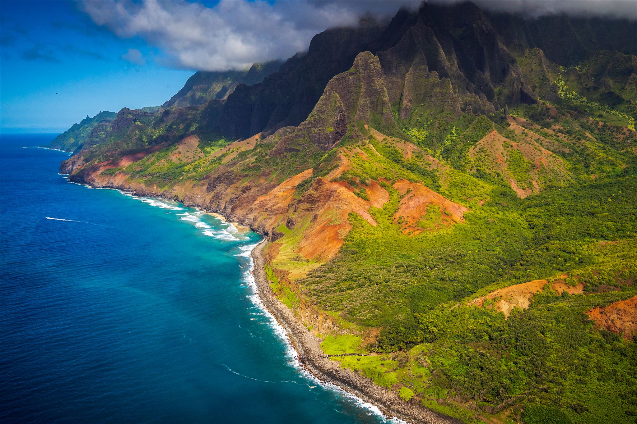 A small boat cruising along the Na Pali Coast on Kauai with dramatic green cliffs and deep blue water under a bright sky