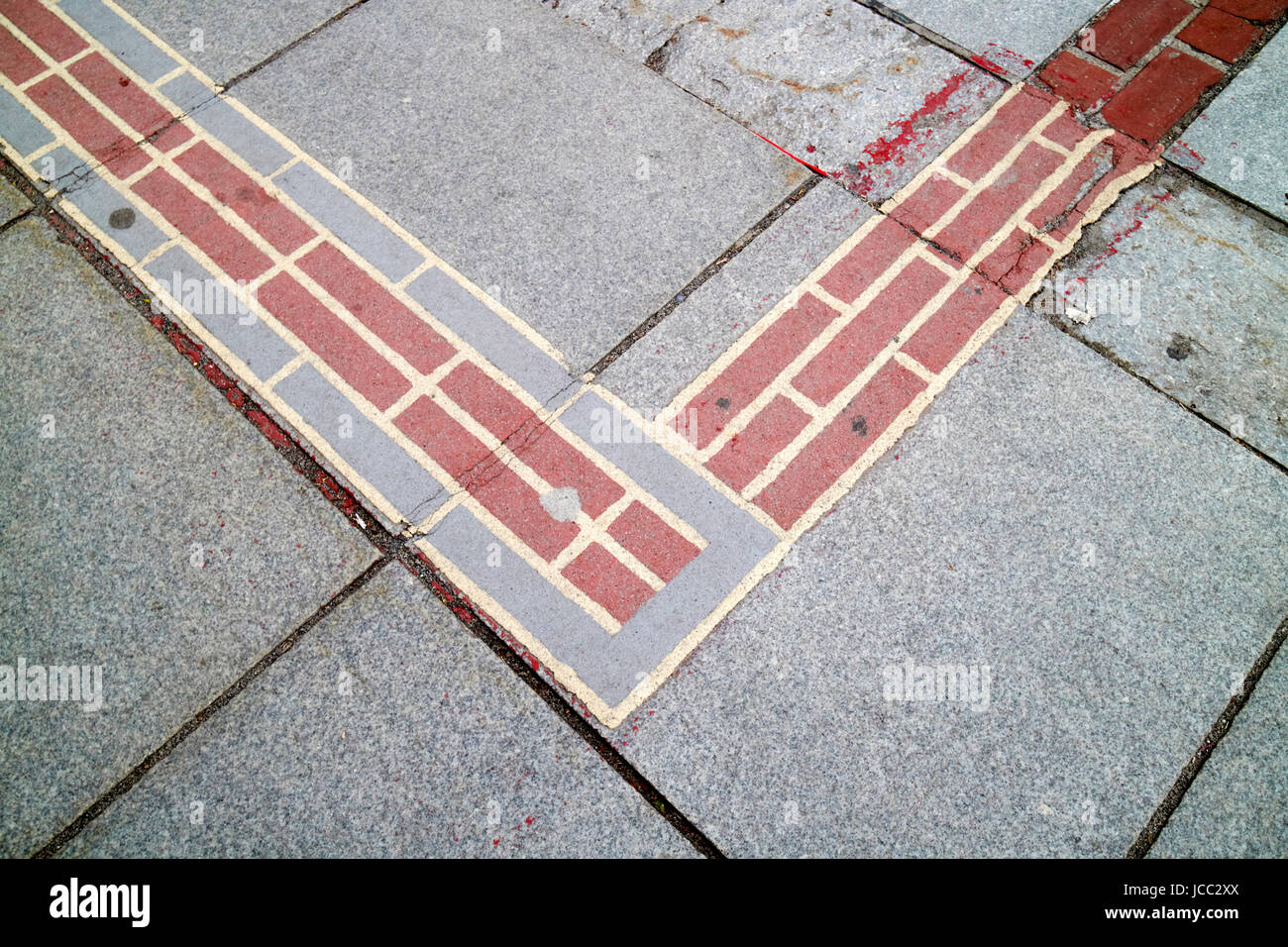 A street-level photograph of the Freedom Trail red brick line leading past historic buildings in downtown Boston on a clear day