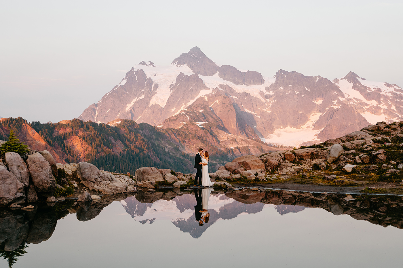 A sunset photograph from Artist Point with Mount Shuksan lit by warm light and hikers silhouetted on a nearby viewpoint