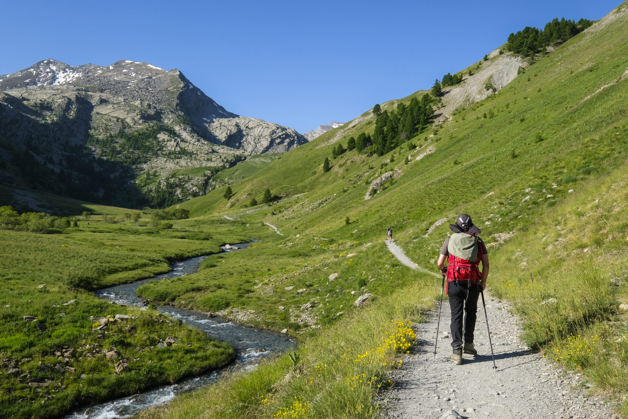A tired hiker sitting on a rocky alpine trail above treeline, stopping to assess symptoms with a backpack and trekking poles beside them, real outdoor photography style
