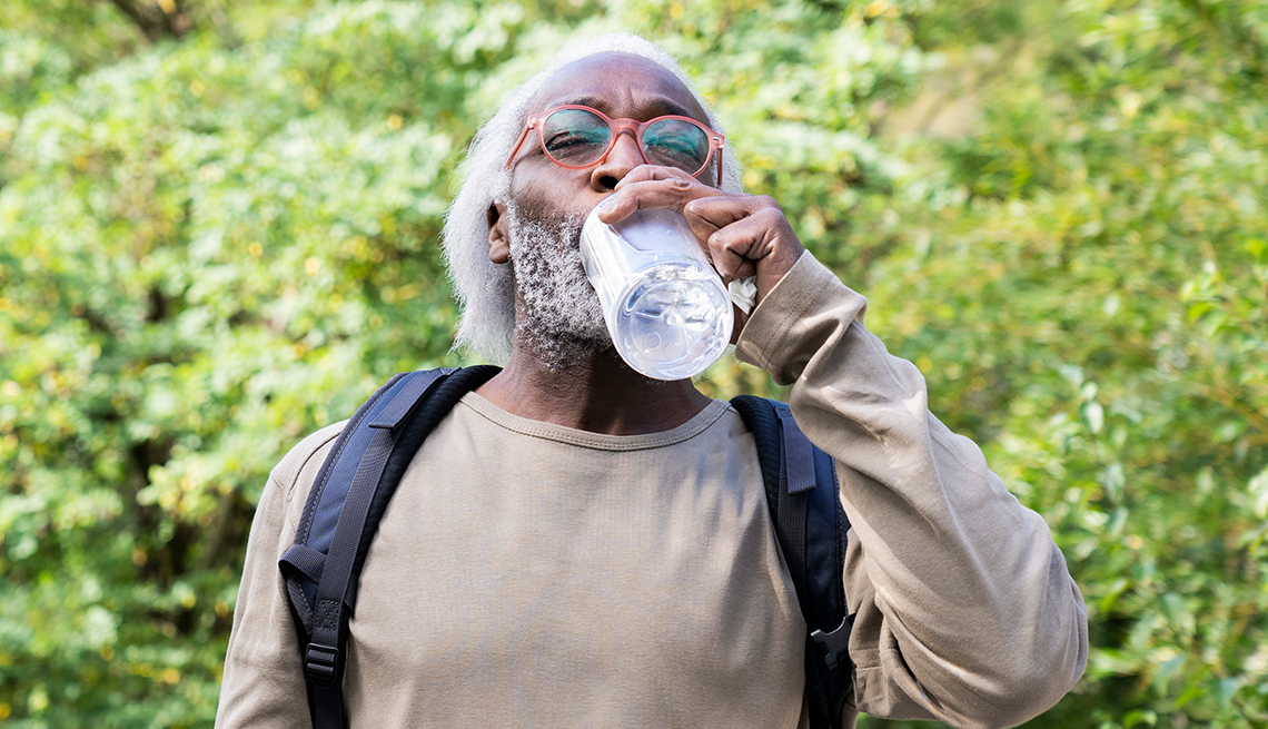 A tired traveler sitting on the edge of a hotel bed in daylight, drinking from a clear bottle of electrolyte water with a small towel nearby, realistic indoor photography