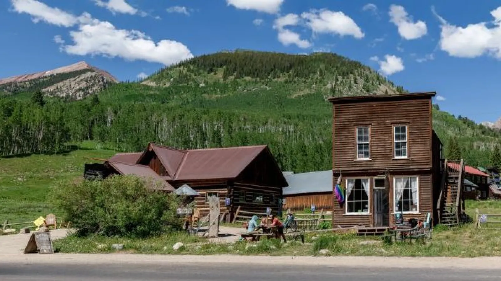 A traveler holding a small cup of coffee while walking past a cozy mountain town cafe in the morning light, realistic travel photography