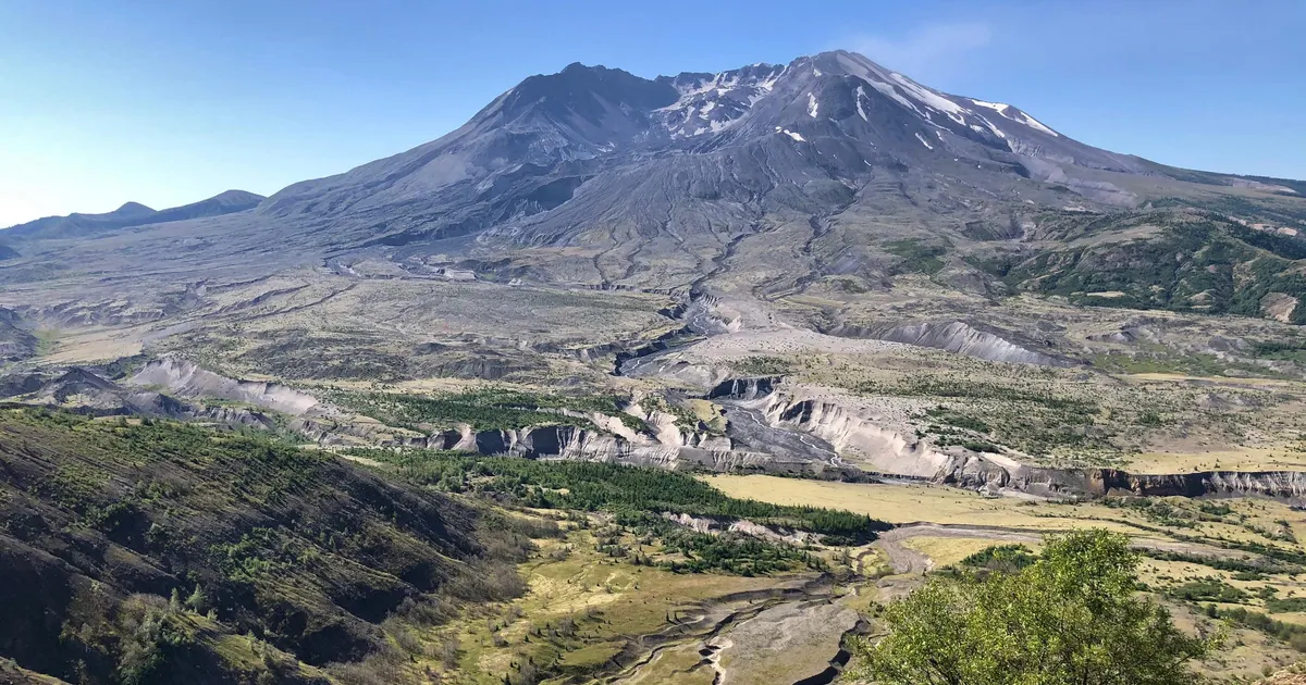 A wide angle photo of visitors walking on a paved interpretive path at Johnston Ridge with Mount St. Helens crater dominating the background
