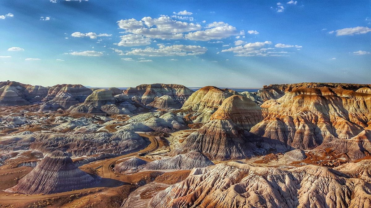 A wide desert overlook in Petrified Forest National Park with layered Painted Desert hills in pink, lavender, and tan under a big Arizona sky, photographed from a viewpoint railing